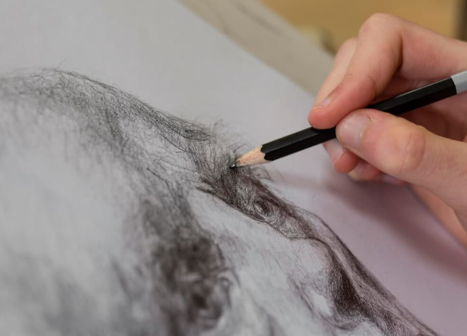 Close-up of a hand drawing an eye with a black pencil on textured paper