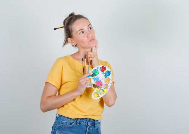 A girl with paints in her hands looks thoughtfully somewhere