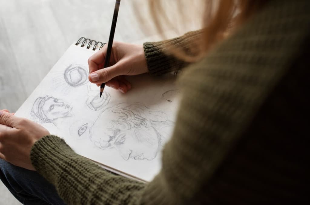 An artist sketches various facial features and a portrait on paper