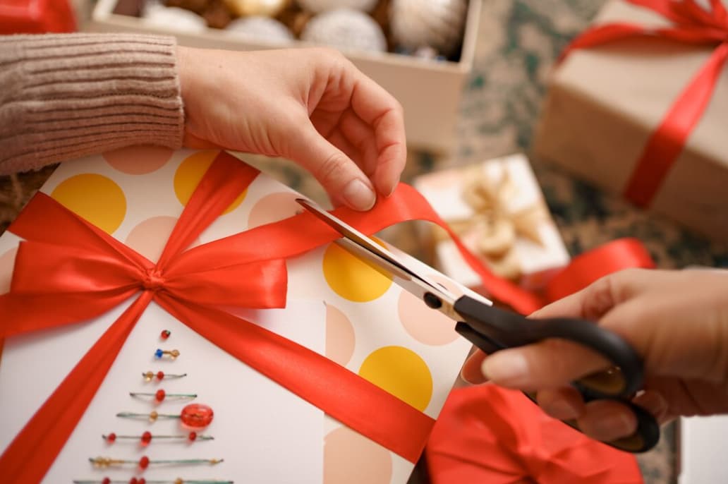 Hands cutting a red ribbon on a wrapped gift with polka dot paper