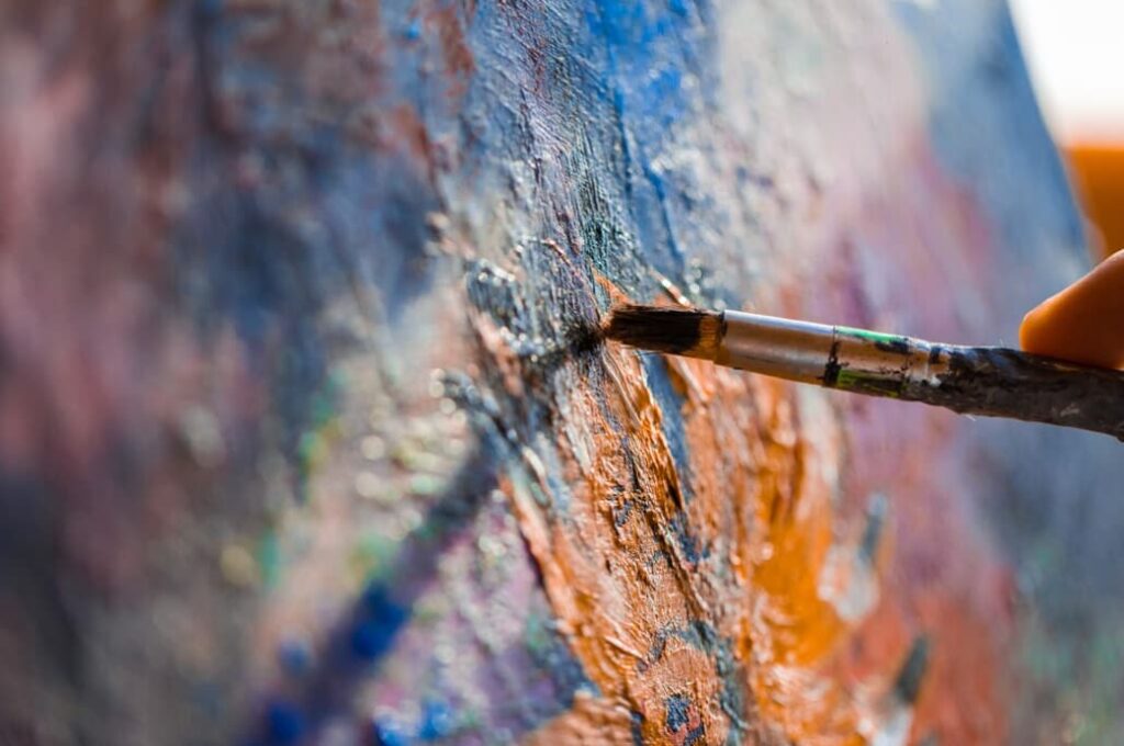 Close-up of a paintbrush applying vibrant paint to a textured canvas